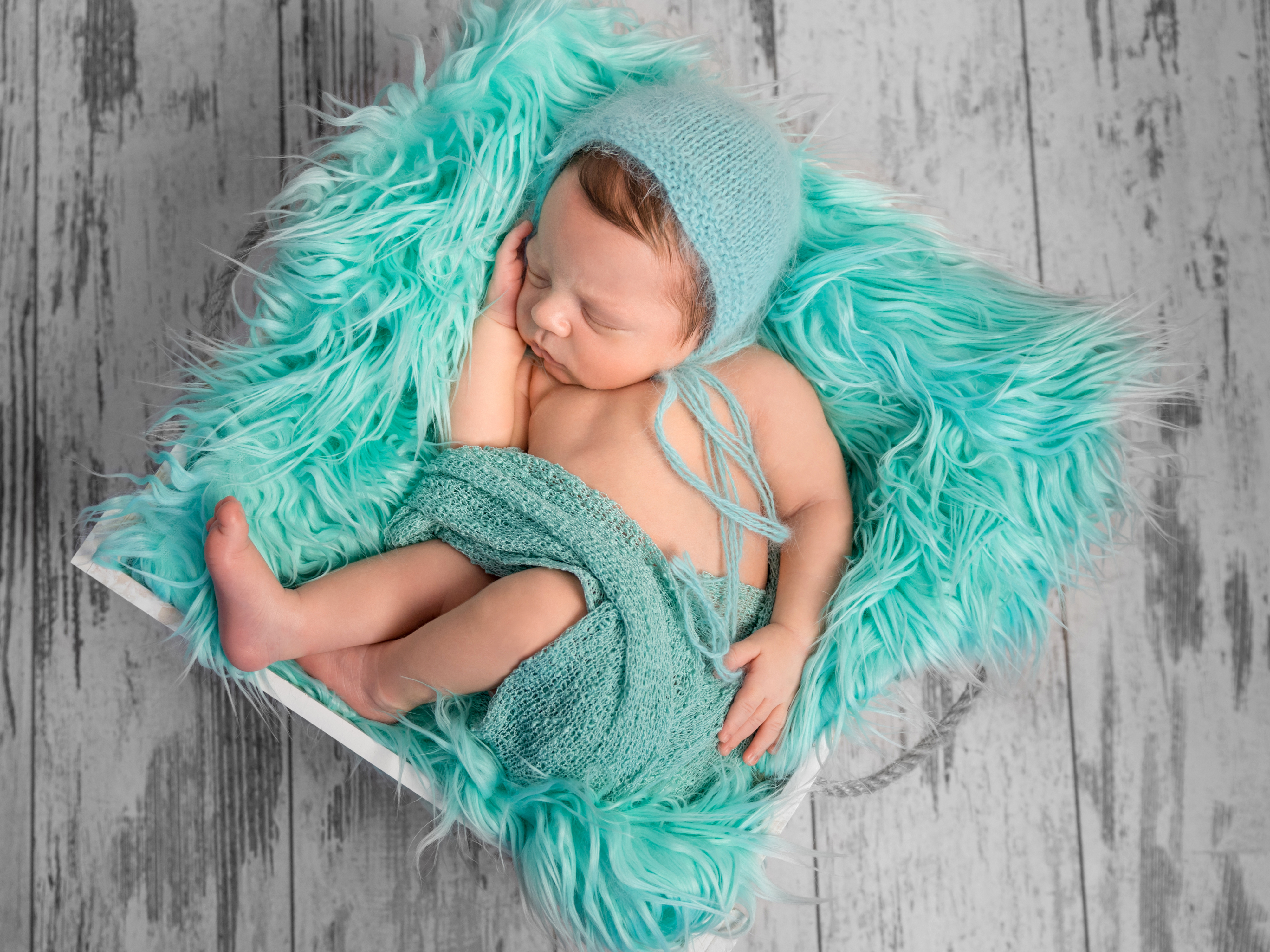 beautiful newborn baby sleeping in hat on square bed with furry turquoise blanket, top view